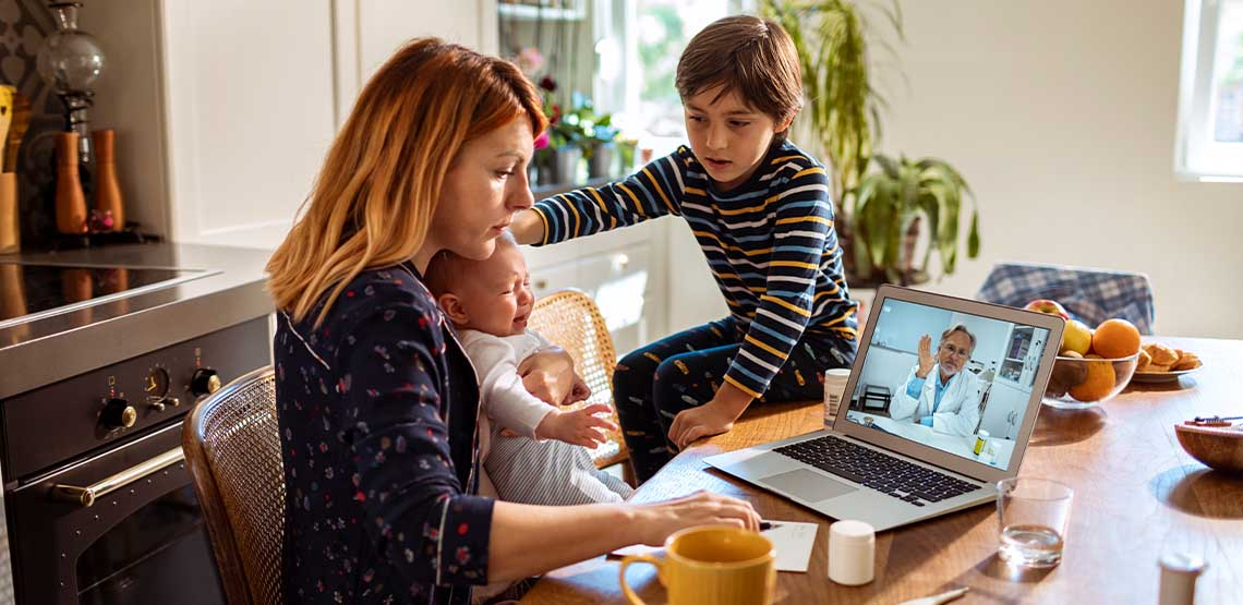 A family sitting at a kitchen table talking to a doctor on a laptop.