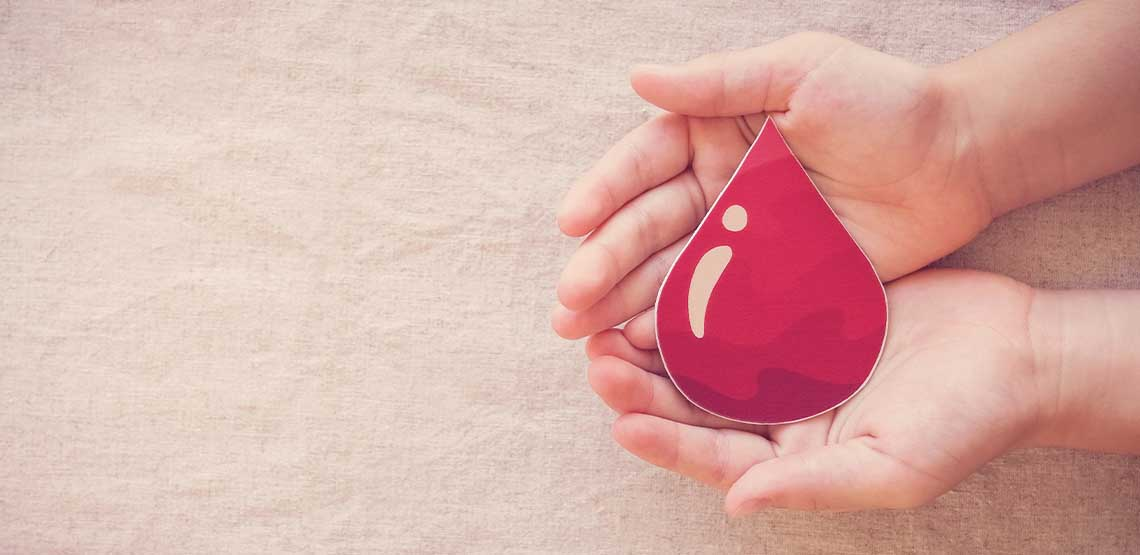 Two hands holding a paper cut out of a drop of blood.