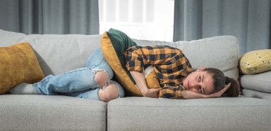 A woman laying on a grey couch in pain.