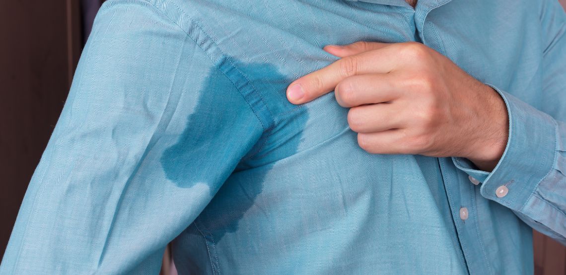 A man looking at the sweat on his shirt, in his underarm area.