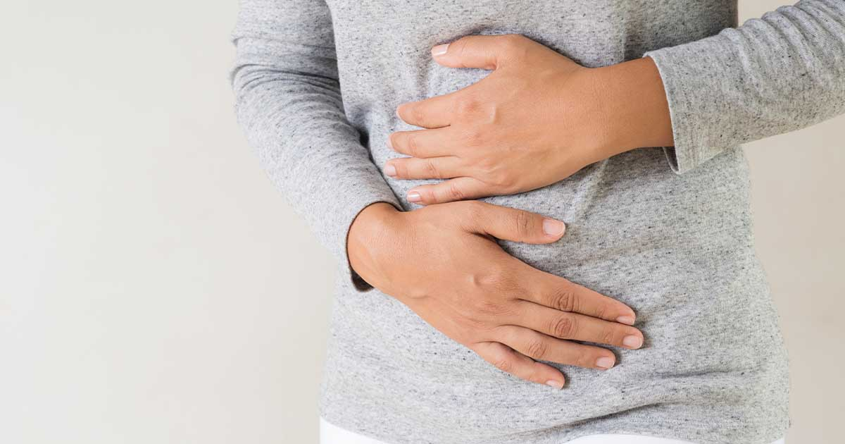 A picture of a woman in a grey sweater, with her hands over her stomach