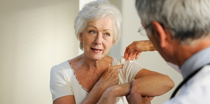 A woman is pointing her to shoulder while her doctor examines it