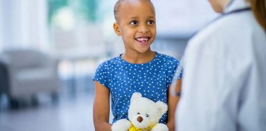 A little girl holding a teddy bear while talking to a doctor.