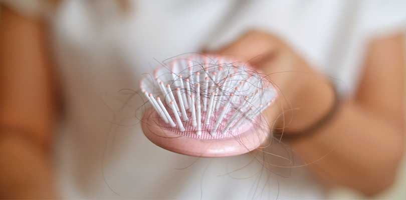 Someone holding a pink brush with excess strands of hair in it.