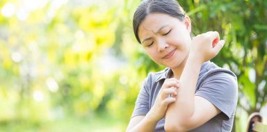 A woman outside itching her arm.