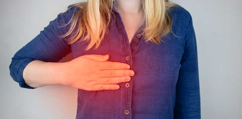 A woman wearing a blue shirt placing a hand over her breast.