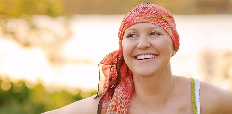 A woman outside smiling while wearing a scarf around her head.