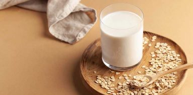 A cup of oat milk with oats on a brown, wooden tray.