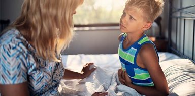 A child clutching his stomach while sitting in bed with him mom.