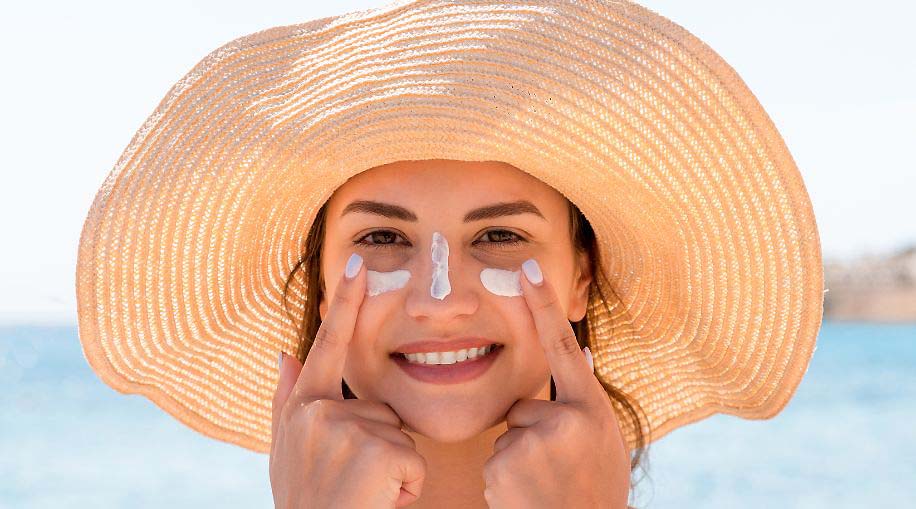 A woman wearing a sun hat with sunscreen under her eyes and on her nose.